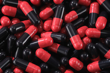 Close-up shots of black and red pills are combined with lighting to create shine and enhance their color. Minimalist space for advertising for pain relievers, treatment drugs, and antibiotics