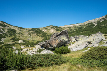 Huge boulders are piled up in the middle of a cirque in Rila Mountains under clear blue sky in summer.