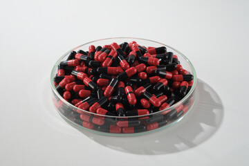High angle shot, mock up photo for advertisement. Red and black medicine is placed in a transparent round petri dish commonly used as a sample for pain reliever drugs