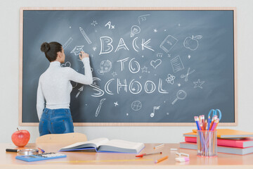 Teacher Writing "Back to School" on Blackboard with School Supplies on Desk in Classroom