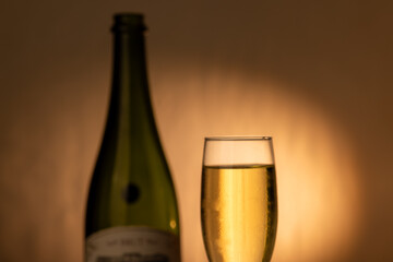 Detailed view of a chilled champagne glass with effervescent bubbles. A green champagne bottle is out of focus on the right, with an elegant gold gradient backdrop, ideal for festive occasions.