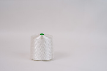 A spool of white fiberglass thread with a green top, displayed against a plain white background, showcasing the texture and weave of the material...