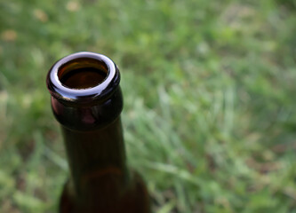 Neck of a brown glass bottle against green grass