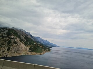 Scenic landscape of  mountains and sea on a cloudy summer day. People hurry up to vacation on of beautiful clean place by the Adriatic Sea. View of the coast of rocky island. Curve road in mountain.