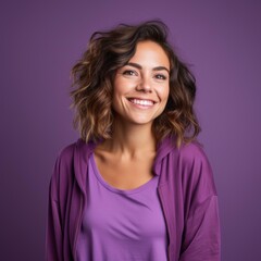Fototapeta premium A young woman with wavy hair smiles confidently, wearing a purple shirt and jacket, against a purple background, ideal for promoting positive emotions, fashion, or lifestyle content,