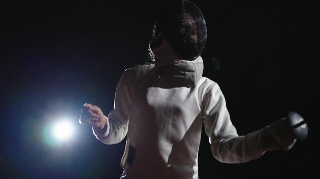 Portrait Of Young Woman Fencer Fighting In Darkness Against Soffit, Her Rival Doing Lunge And Touche