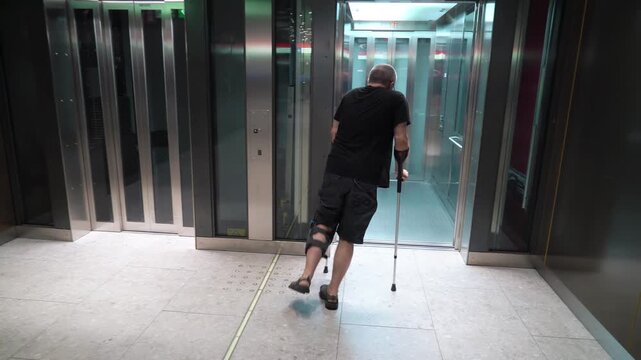 Mature man with bondage, medical splint, knee brace on the leg going to elevator using crutches. Accessible urban environment for the disabled, recovery from injury.