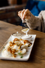 handsome girll is eating Delicious juicy dumplings with fragrant herbs and cracklings, served with buttery sauce and sour cream in a beautiful dish on a wooden table in a cozy, charming restaurant