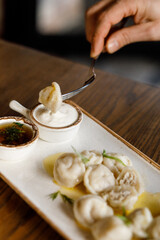 handsome girll is eating Delicious juicy dumplings with fragrant herbs and cracklings, served with buttery sauce and sour cream in a beautiful dish on a wooden table in a cozy, charming restaurant