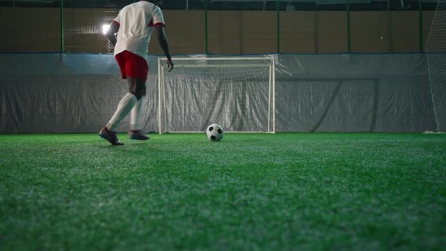 Black soccer player exercising penalty in training hall, scoring goal, back view