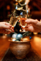 small, beautiful girl and a handsome man are holding two glasses of delicious champagne in front of a Christmas tree in a cozy, charming restaurant