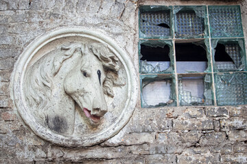 White horse's head sculpture near a broken thick glass window in weathered brick wall