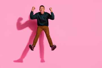 Full length photo of lucky funny guy wear sweatshirt jumping high rising fists emtpy space isolated...