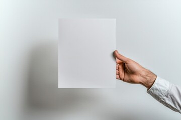 Obraz premium A man's hand firmly grasping a blank white poster mockup against a plain background, ideal for design presentations.