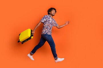 Full body photo of attractive young man running hold baggage dressed stylish colorful clothes isolated on orange color background