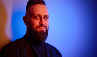 Studio portrait with colorful light of young handsome bearded man.