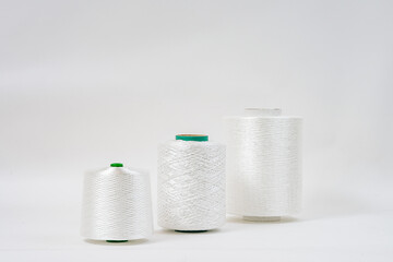  Three spools of white fiberglass yarn in different sizes are aligned in a row against a plain background, showcasing their texture and form.