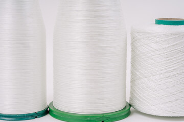Close-up view of three spools of white fiberglass yarn, showcasing their texture and detail, with a plain white background.