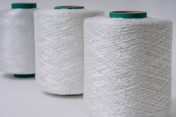 Close-up of three spools of white fiberglass yarn arranged in a row, showcasing their texture and weave patterns against a white background.