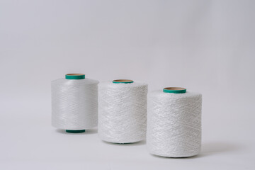 Three spools of white fiberglass yarn are arranged in a diagonal line on a white background, highlighting their texture and material.