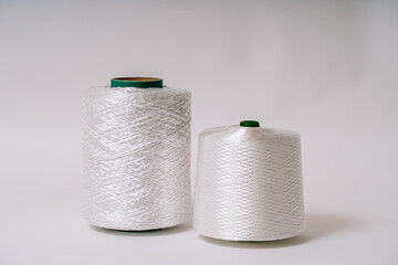 Two spools of white fiberglass thread, showcasing different textures and sizes, placed side by side against a plain background.