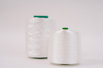 Two spools of white fiberglass thread, with green cores, stand side by side against a plain white background, showcasing their smooth texture.