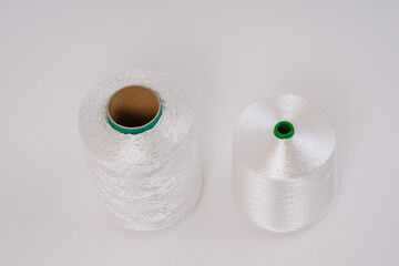 Two spools of white fiberglass thread, one taller with a visible cardboard core and the other shorter with a green plastic core, on a white background.