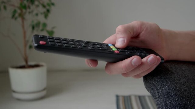 Side closeup of hand of unrecognizable person pressing not working buttons of broken tv remote control indoors