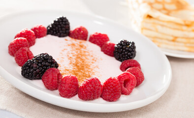 Breakfast of raspberries and blackberries with yogurt and pancakes on table