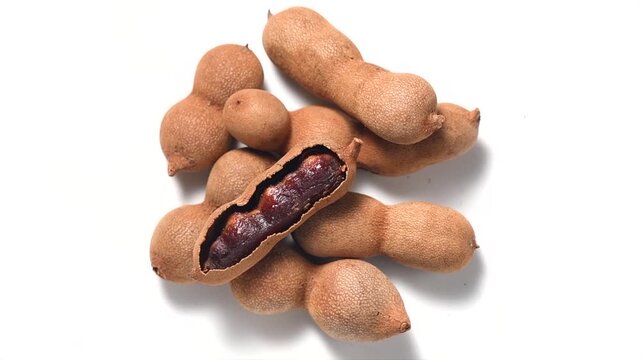 Tamarind tropical fruits isolated on white background. Heap Fresh ripe dryed Tamarind pods (Tamarindus indica, Indian date), healthy vegan food. Top view, flat lay, rotating, slow motion