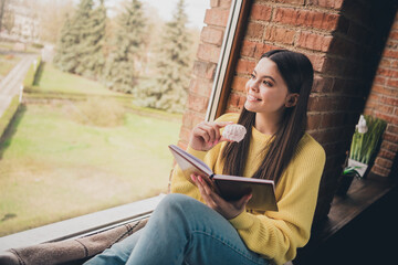 Obraz premium Photo portrait of nice teen lady read book sit windowsill eat snacks dressed yellow garment spend pastime spacious house indoors room