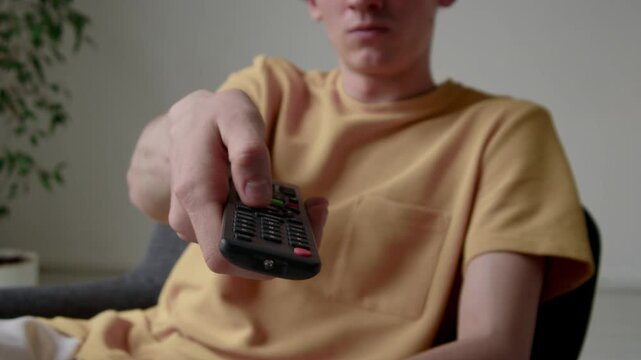 Cropped shot of young guy in mustard t-shirt using broken television remote at home
