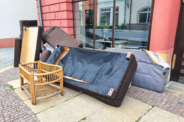 A pile of discarded furniture including a sofa, chair, and various cushions on a city sidewalk,...