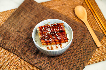 Teriyaki eel donburi with rice, chopsticks and spoon served in bowl isolated on napkin side view of Japanese food