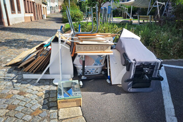A heap of assorted discarded household items and furniture piled up on a cobblestone street,...