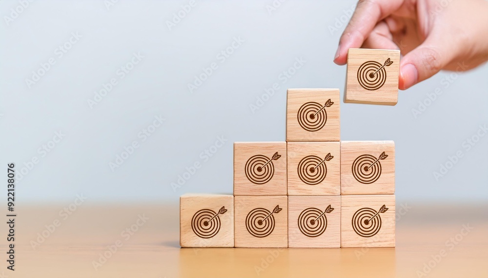 Poster hand holding wooden block with target aiming dart board and arrow up on table background. business a