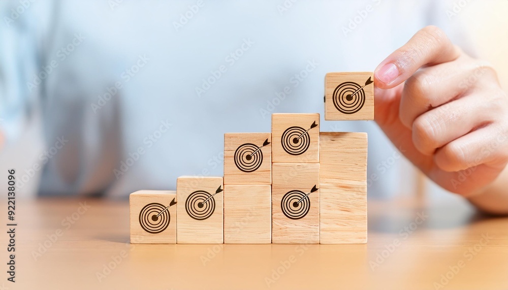 Poster hand holding wooden block with target aiming dart board and arrow up on table background. business a
