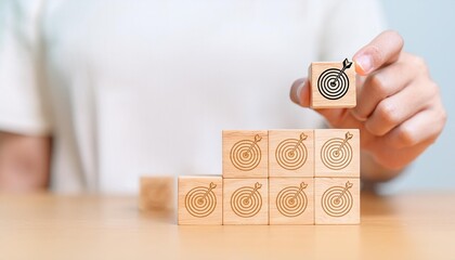 Hand holding wooden block with target aiming dart board and arrow up on table background. Business achievement objective goal and project progress growth value processing marketing financial concept