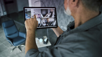 Male installer watches CCTV cameras in stylish office using tablet computer. Real time view of surveillance cameras displayed on tablet screen. Monitoring and tracking. Security system and privacy.