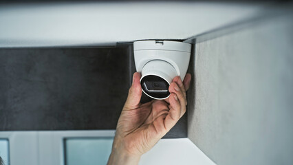 Professional male installer screws CCTV camera to the ceiling in office room using screwdriver tool...