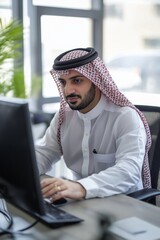 A man wearing a white shirt and a red and white scarf is sitting in front of a computer