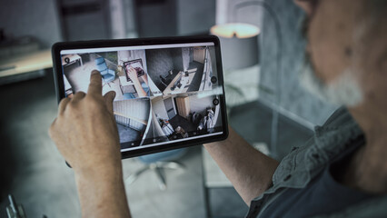 Male mature technician watches and controls CCTV cameras in modern office using tablet computer....