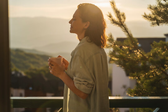 Young woman greeting the morning and sunrise standing on a balcony overlooking the mountains