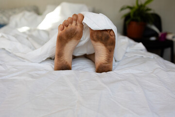 A cozy morning scene depicts relaxed very dirty feet comfortably peeking out from under a soft bed cover, creating warmth