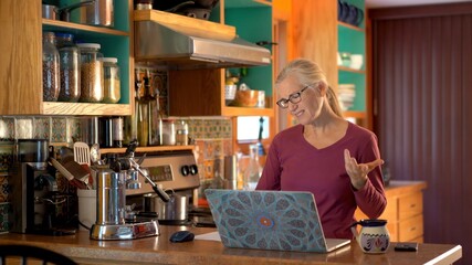 Mature woman unhappy working on computer at home on kitchen counter.