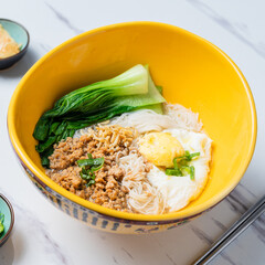 A vibrant yellow bowl of Asian noodles topped with minced pork, poached egg, and bok choy, served...