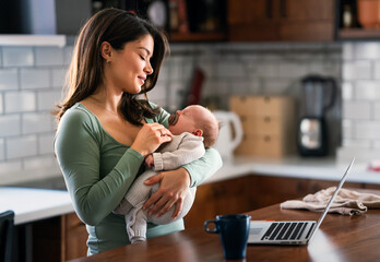 Stay at home mom working remotely on laptop while taking care of her baby. Global work on computer