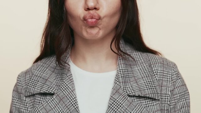Close-up of a young woman making a humorous face by puffing her cheeks, expressing playfulness and joy on a muted background.