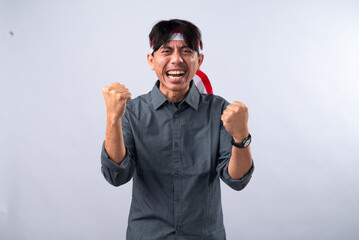 Indonesian man celebrating with fists raised, wearing a grey shirt and a red-and-white headband. He...