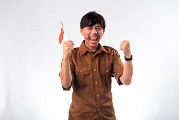 Indonesian man in a brown uniform shirt, smiling and cheering while holding an Indonesian flag. He...